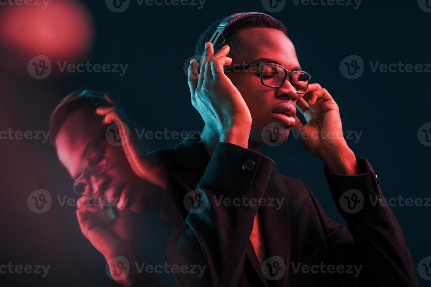 Enjoying listening music in headphones. In glasses. Futuristic neon lighting. Young african american man in the studio photo