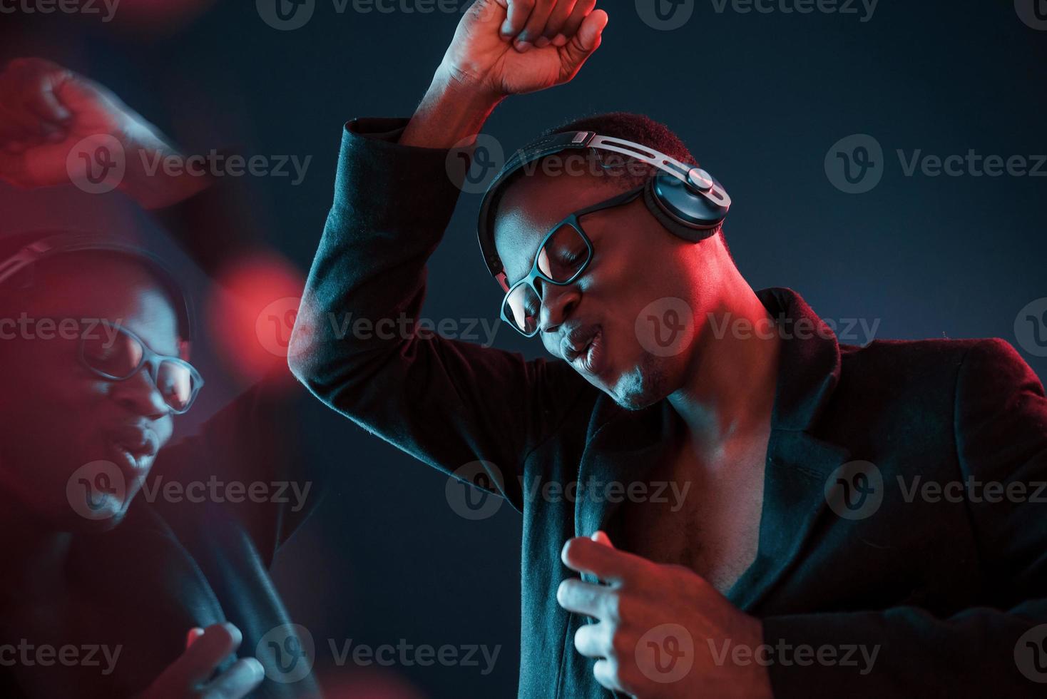 Enjoying listening music in headphones. In glasses. Futuristic neon lighting. Young african american man in the studio photo