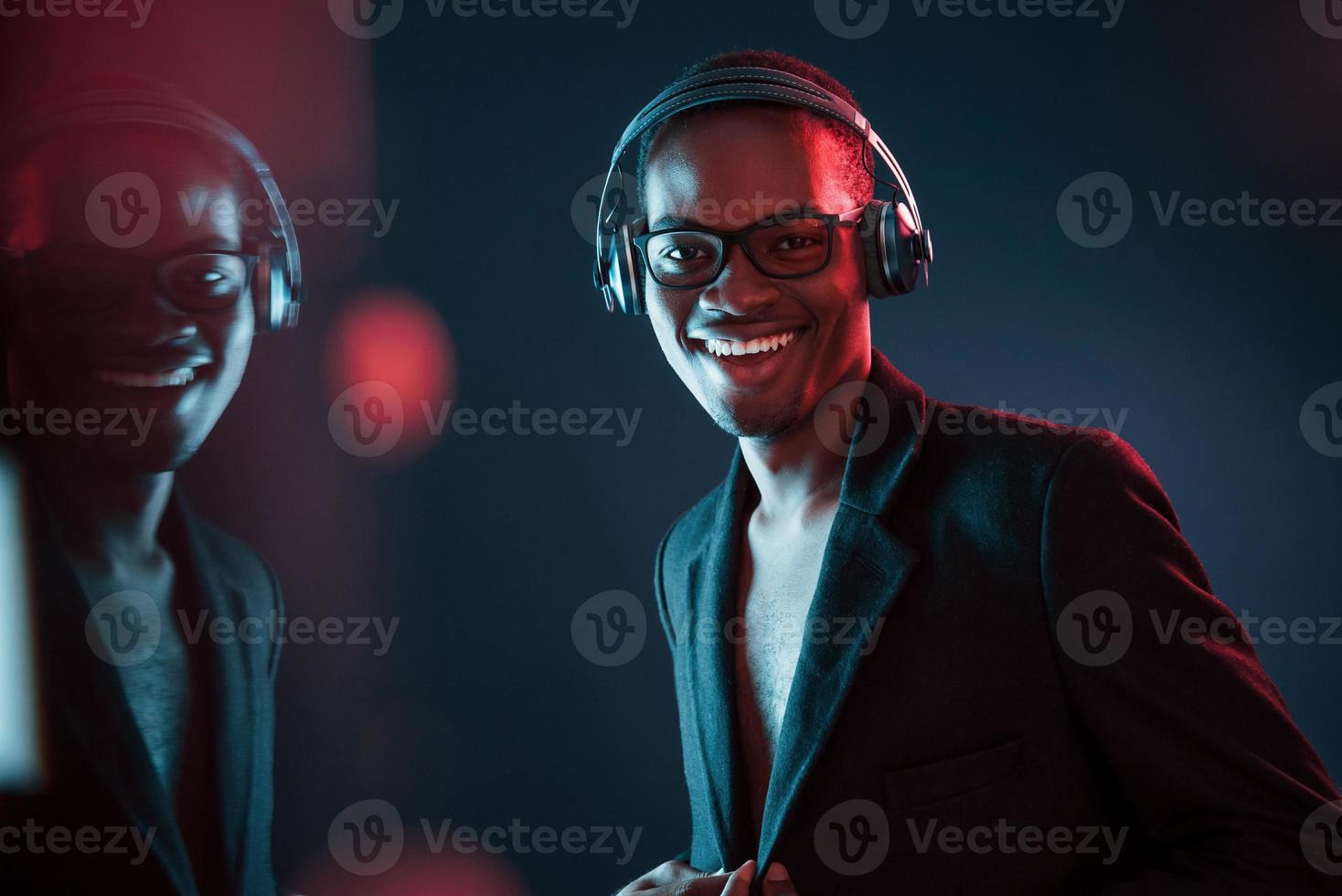 Enjoying listening music in headphones. In glasses. Futuristic neon lighting. Young african american man in the studio photo