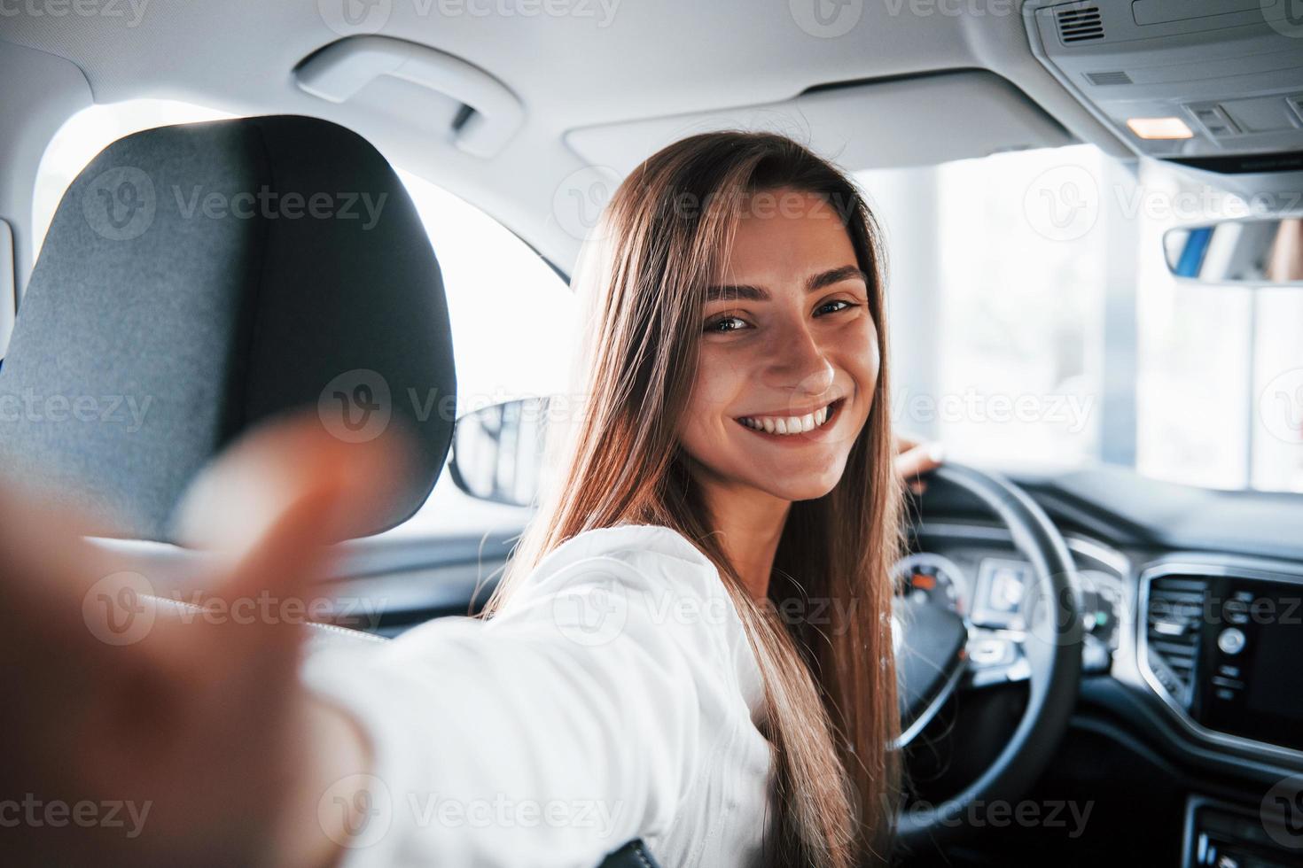 Making selfie. Cheerful female driver is in her new car. Interior of modern automobile photo