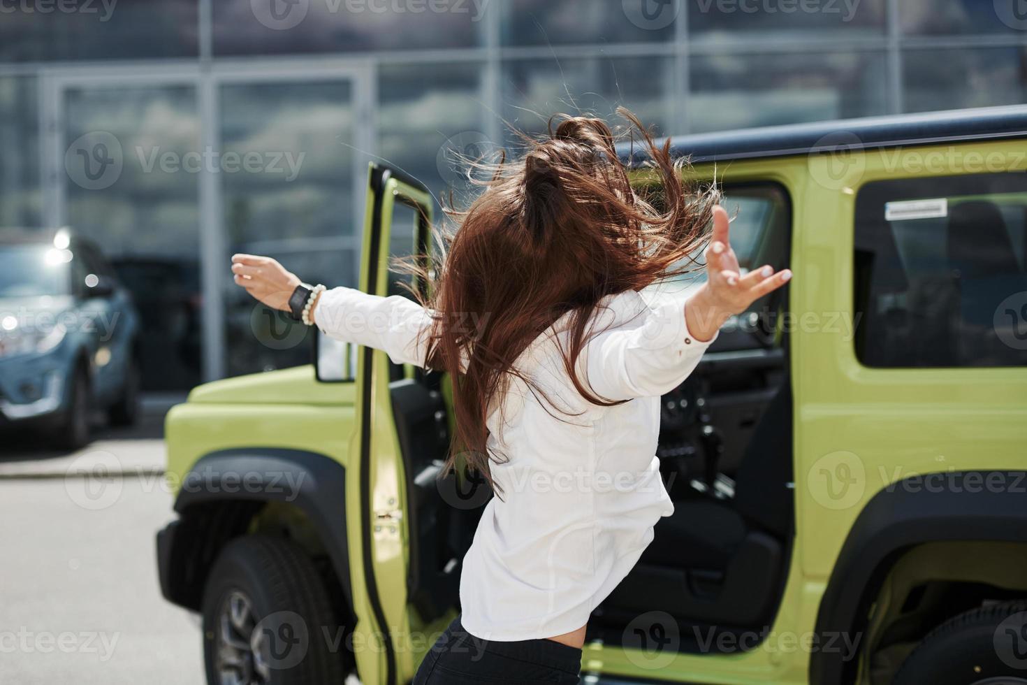 Young woman in white official clothes dancing in front of hew new green automobile outdoors photo