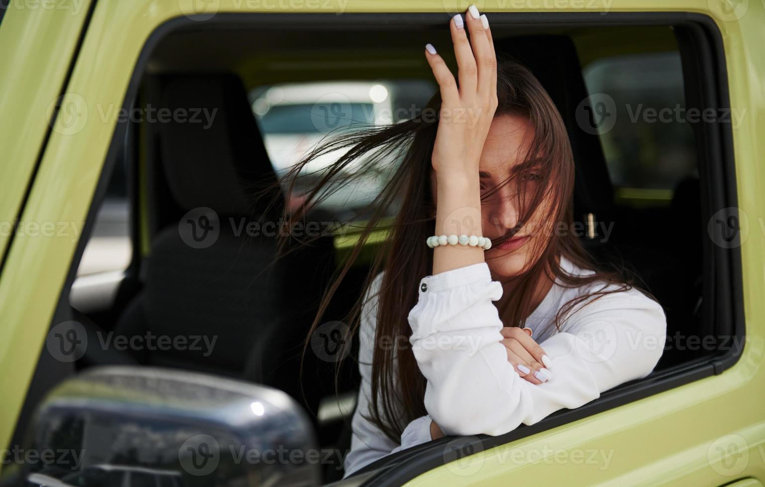 Young woman sits in green colored car and looks through the door photo