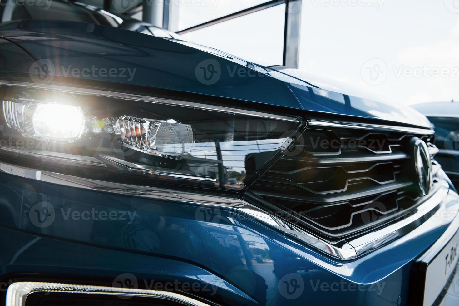 Front part of brand new modern blue car. Parked at showroom. Reflection in the headlights photo