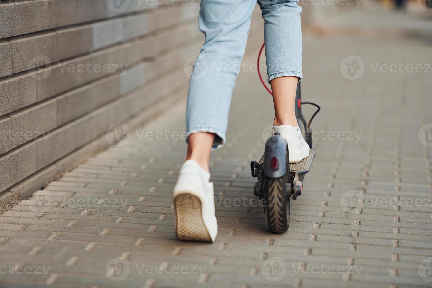 Close up view of girl in casual clothes that riding electric schooter outdoors at sunny daytime photo