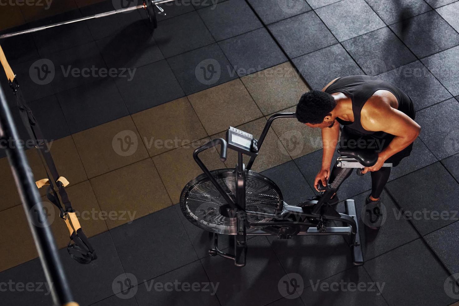 Riding bicycle. Strong african american man in sportive clothes have workout day in the gym photo