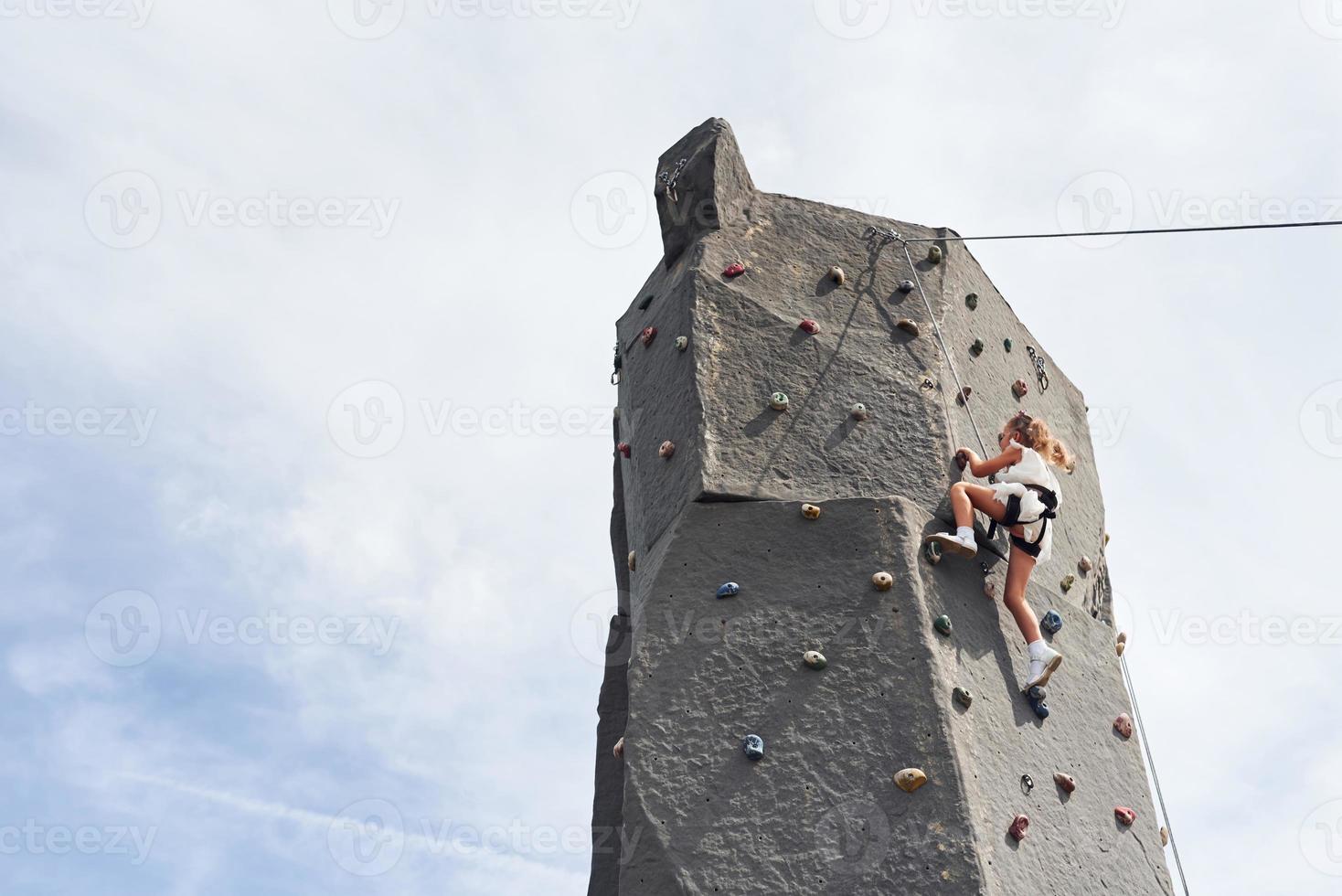 Little girl in casual white clothes training rock climbing outdoors photo