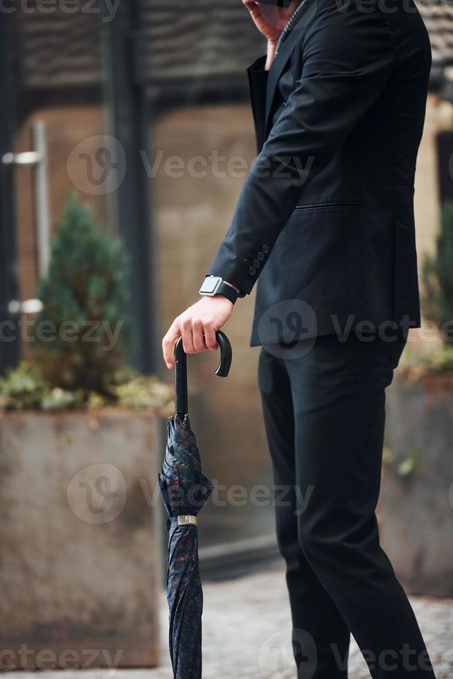 Close up view. Holding umbrella. Elegant young man in formal classy