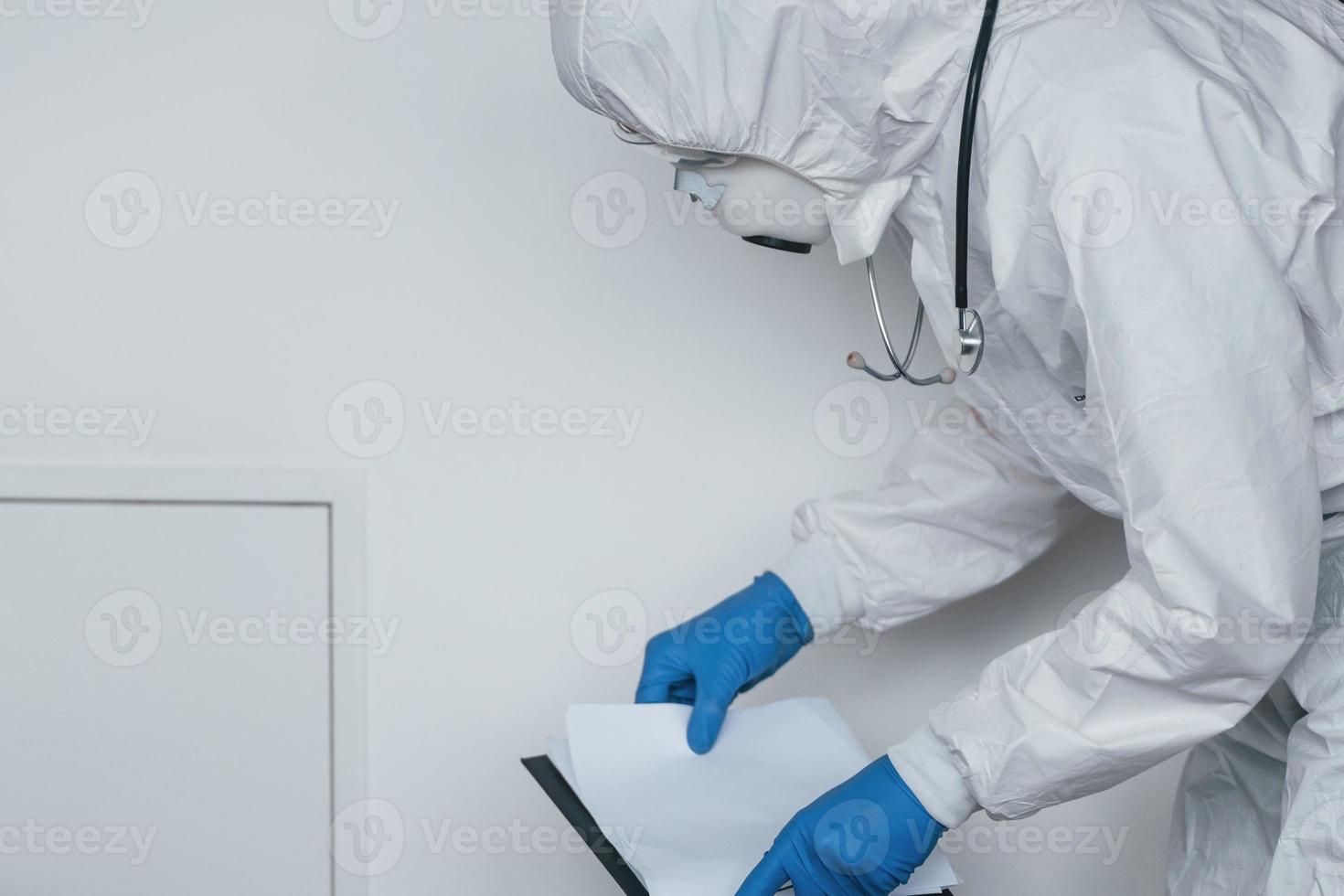 Male doctor scientist in lab coat, defensive eyewear and mask holding notepad in hands photo