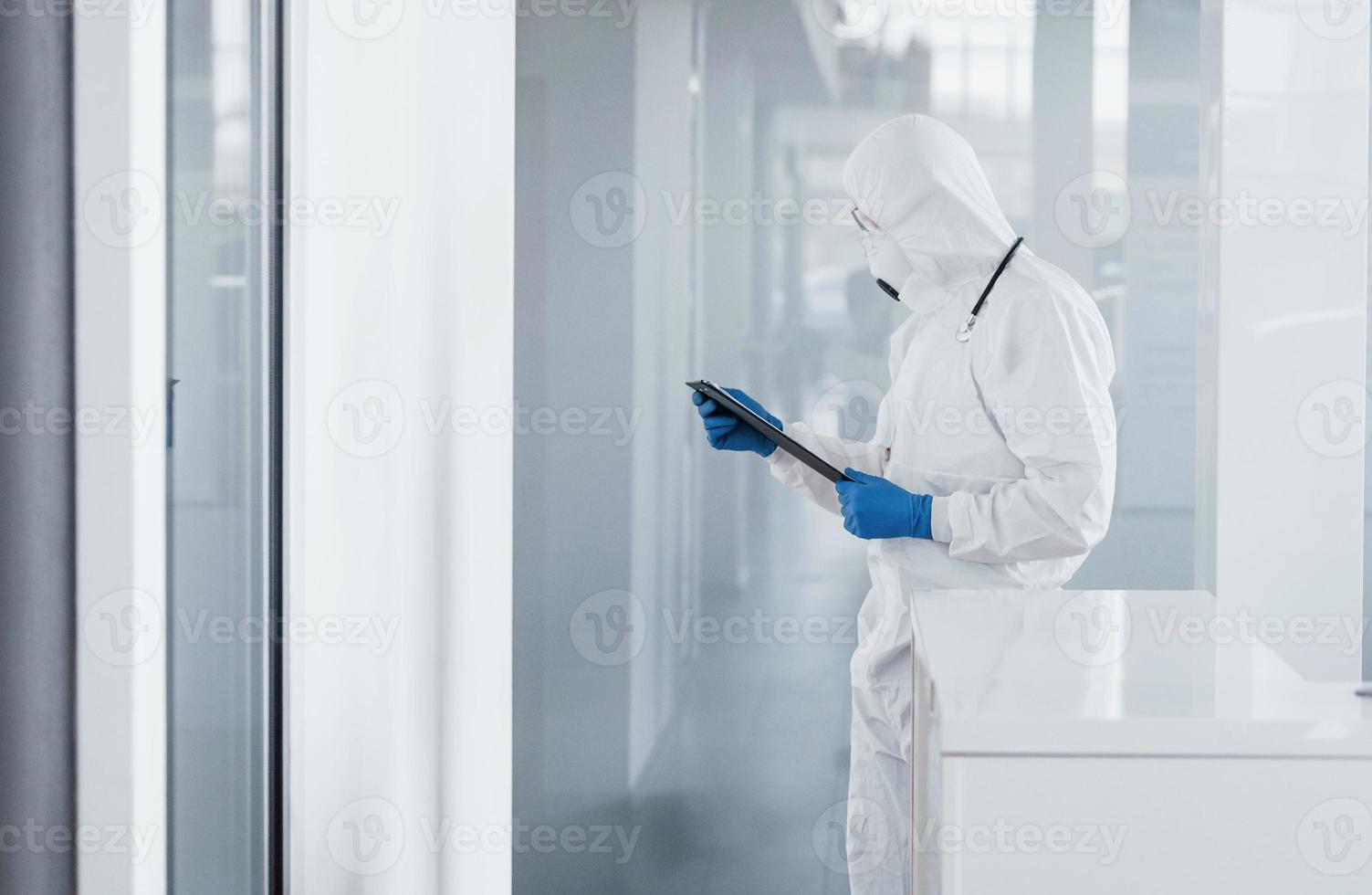 Male doctor scientist in lab coat, defensive eyewear and mask holding notepad in hands photo