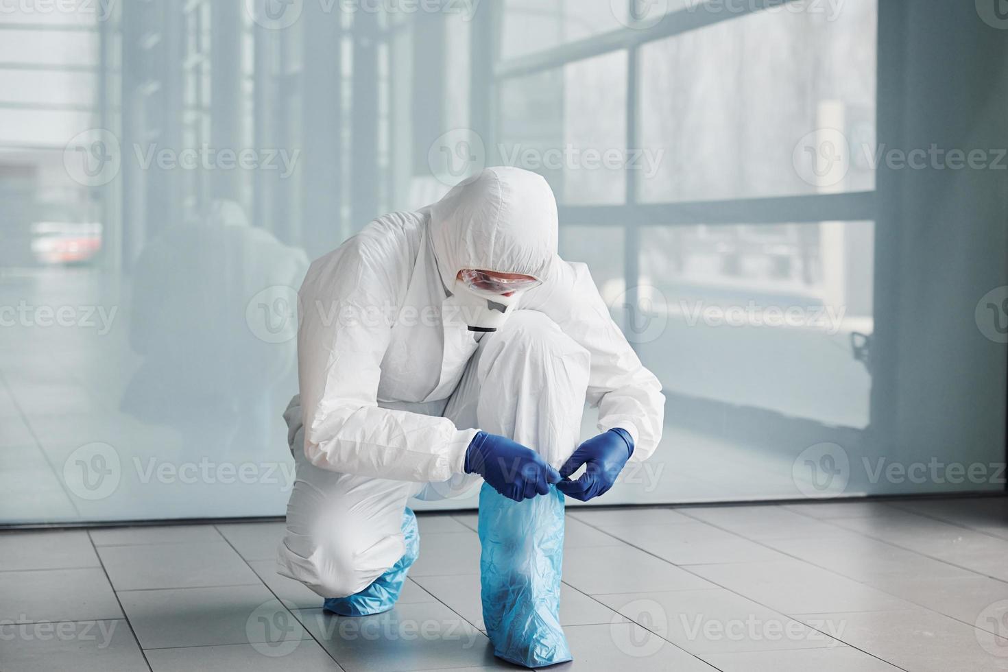 Male doctor scientist in lab coat, defensive eyewear and mask wearing protective material on legs photo