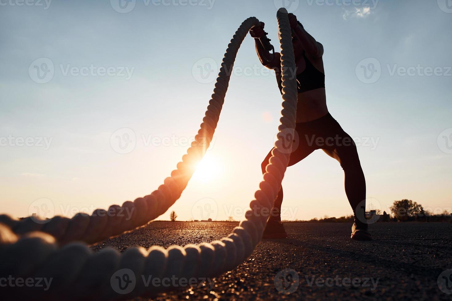 Woman in sportswear training with knots on the road at evening time photo