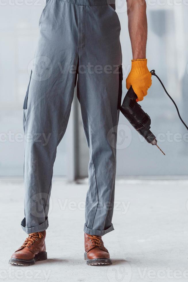 Close up view of man in grey uniform with drill in hand indoors in modern big office at daytime photo