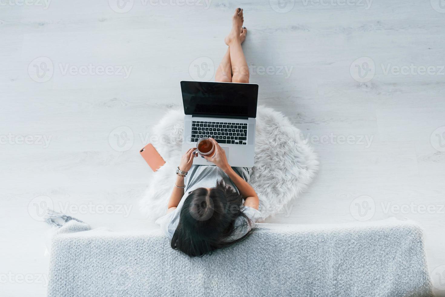 Top view of young woman in casual clothes that sitting at home alone with laptop and tea photo