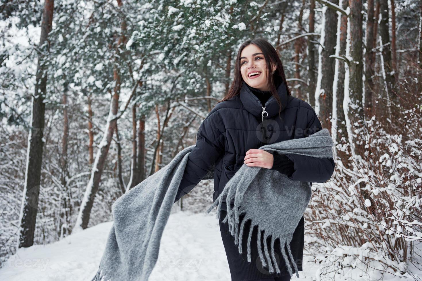 Having some fun. Portrait of charming woman in the black jacket and grey scarf in the winter forest photo