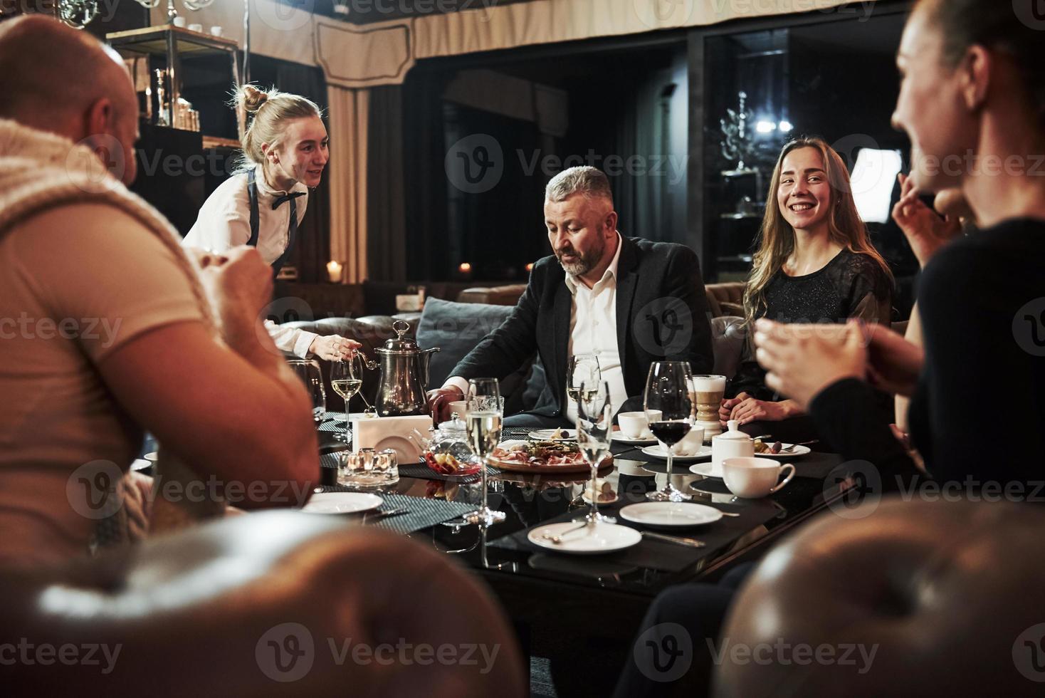 Talking with female waiter. Family friends having nice time in beautiful luxury modern restaurant photo