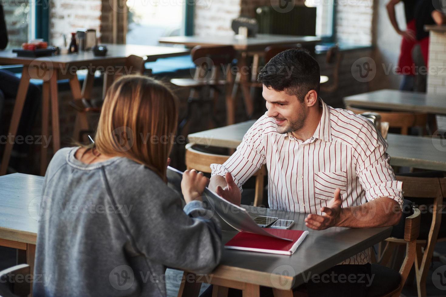 mirando los resultados del trabajo y sonriendo. la gente tiene conversación en el restaurante. hombre con camisa a rayas habla con una chica foto