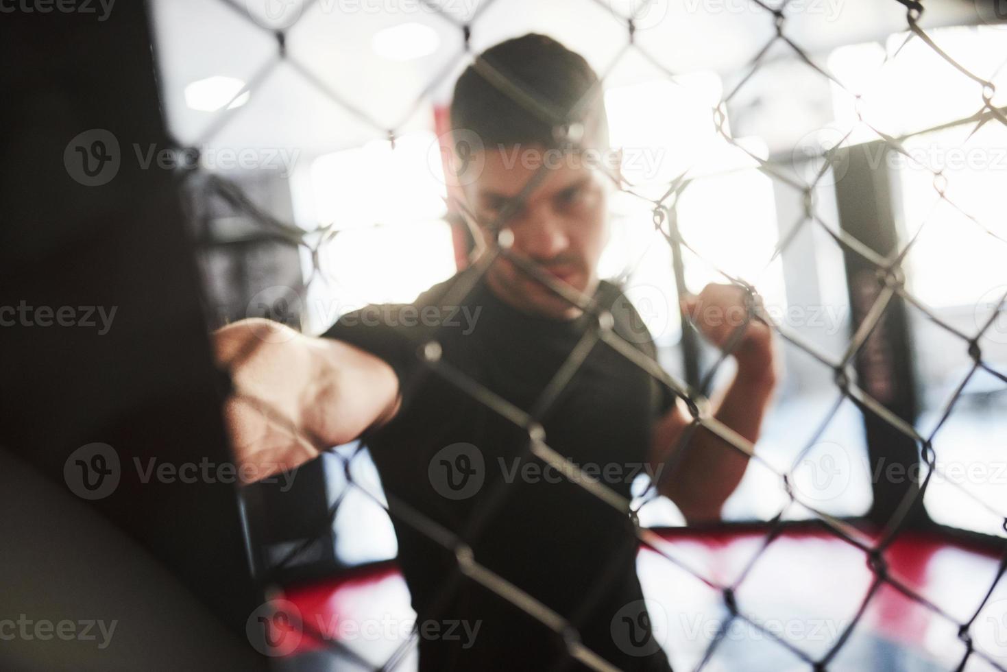 Blurred picture. Strong man is boxing in the gym behind the fence. Haves daily exercise photo