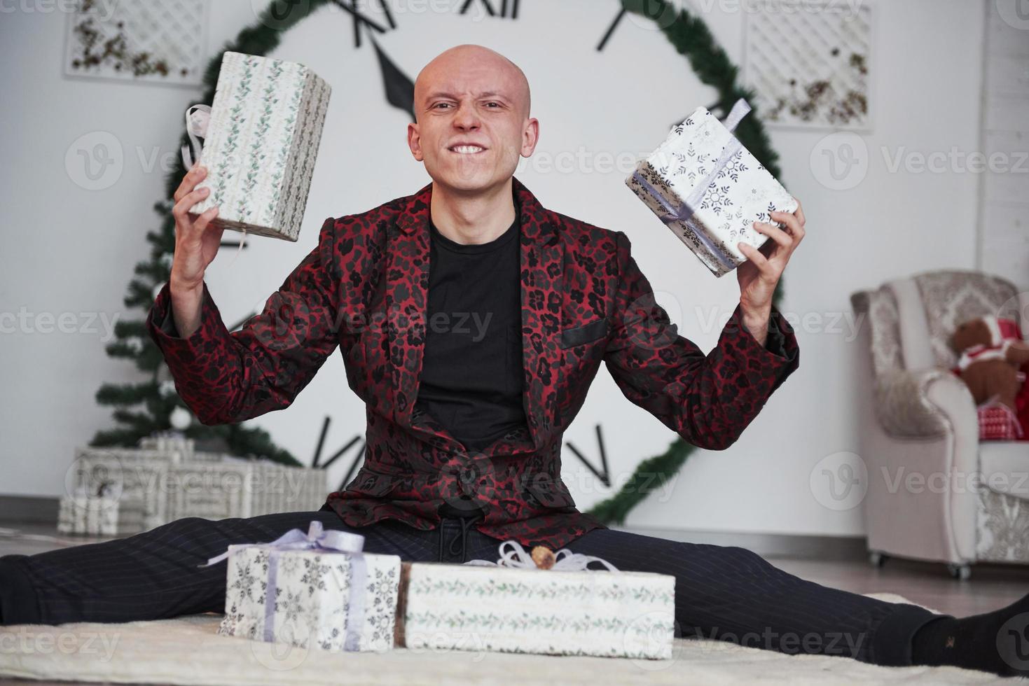 Look what I have. Man with big clock behind him sitting with New year gift boxes in holiday clothings photo