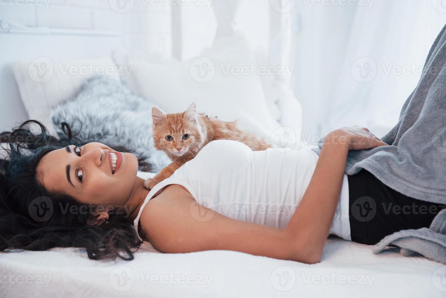 Animal and human friendship. Attractive blonde resting on the white bed with her cute kitten photo