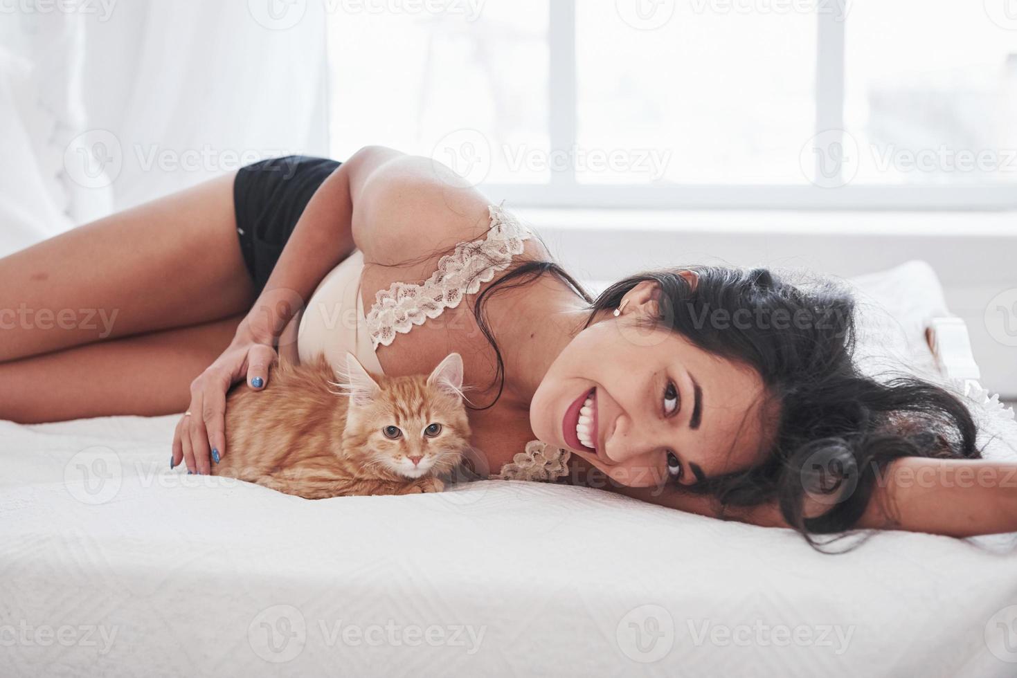 Lying together. Attractive blonde resting on the white bed with her cute kitten photo
