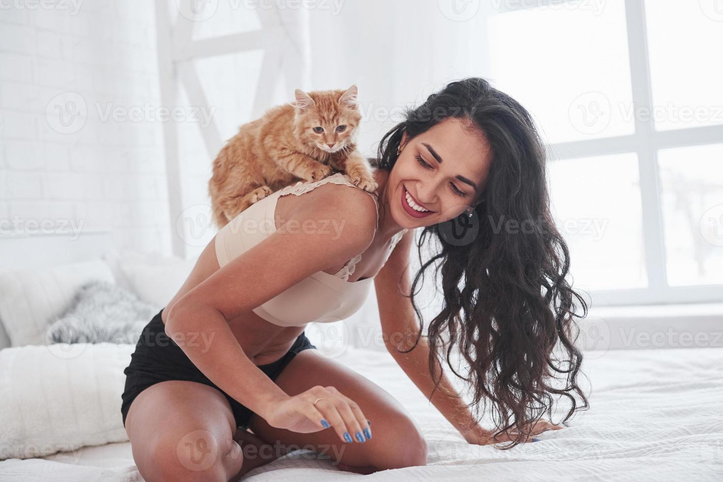 Playful kitten is on the shoulders. Girl have weekend sitting on the bed. Brunette resting on the couch photo