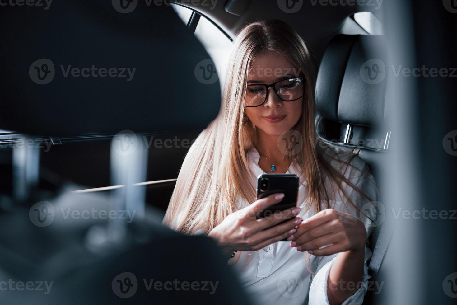 tecnologías inalámbricas. mujer de negocios inteligente se sienta en el asiento trasero del coche de lujo con interior negro foto