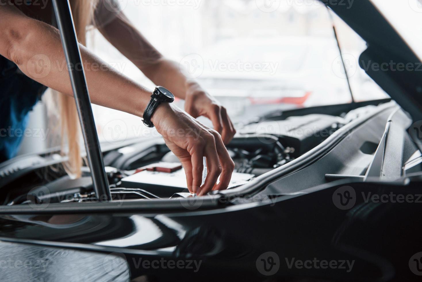 Watch in focus. On the lovely job. Car addicted woman repairs black automobile indoors photo