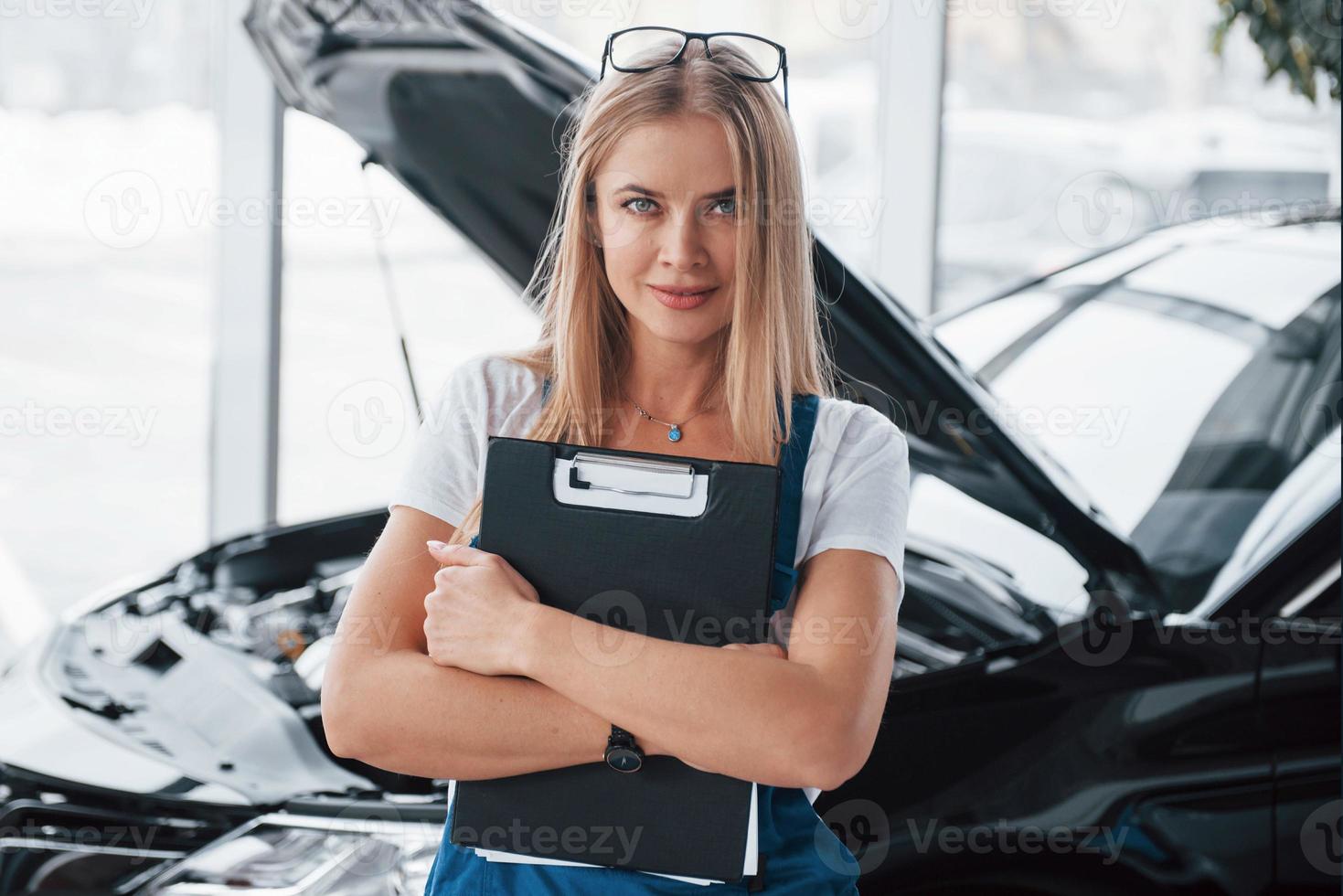 Manager with notepad, in the white shirt and blue uniform stands against automobile with hood up photo