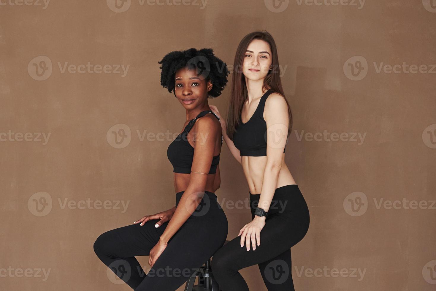 Fashion models. Two multi ethnic female friends stands in the studio with brown background photo