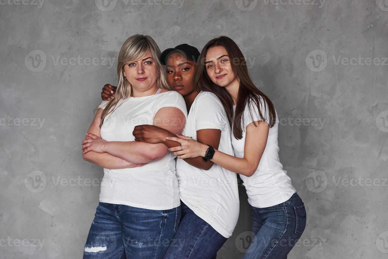 In same clothes. Group of multi ethnic women standing in the studio against grey background photo