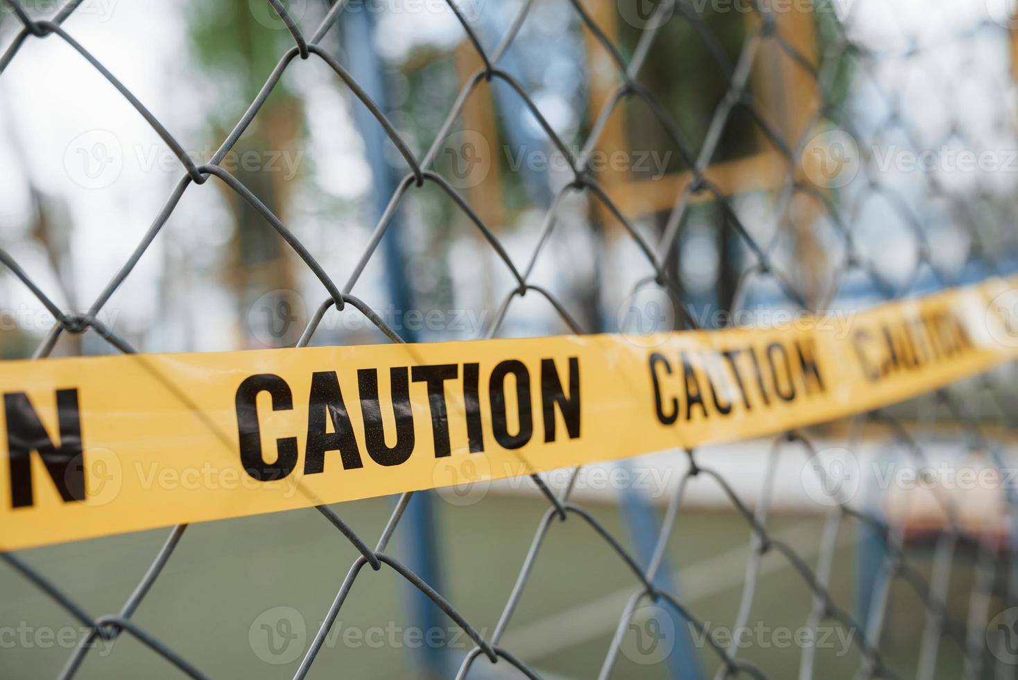 Yellow caution tape on the metal fence at daytime. Crime scene photo