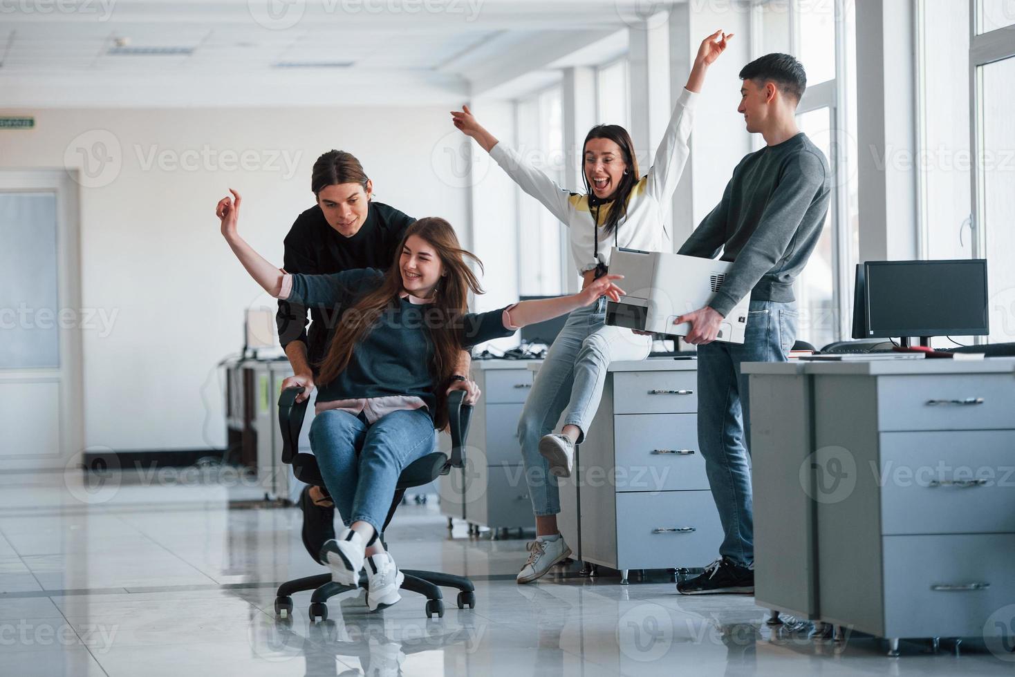 Man holds printer. Having fun in the office. Young people have a break and driving by using a seat photo