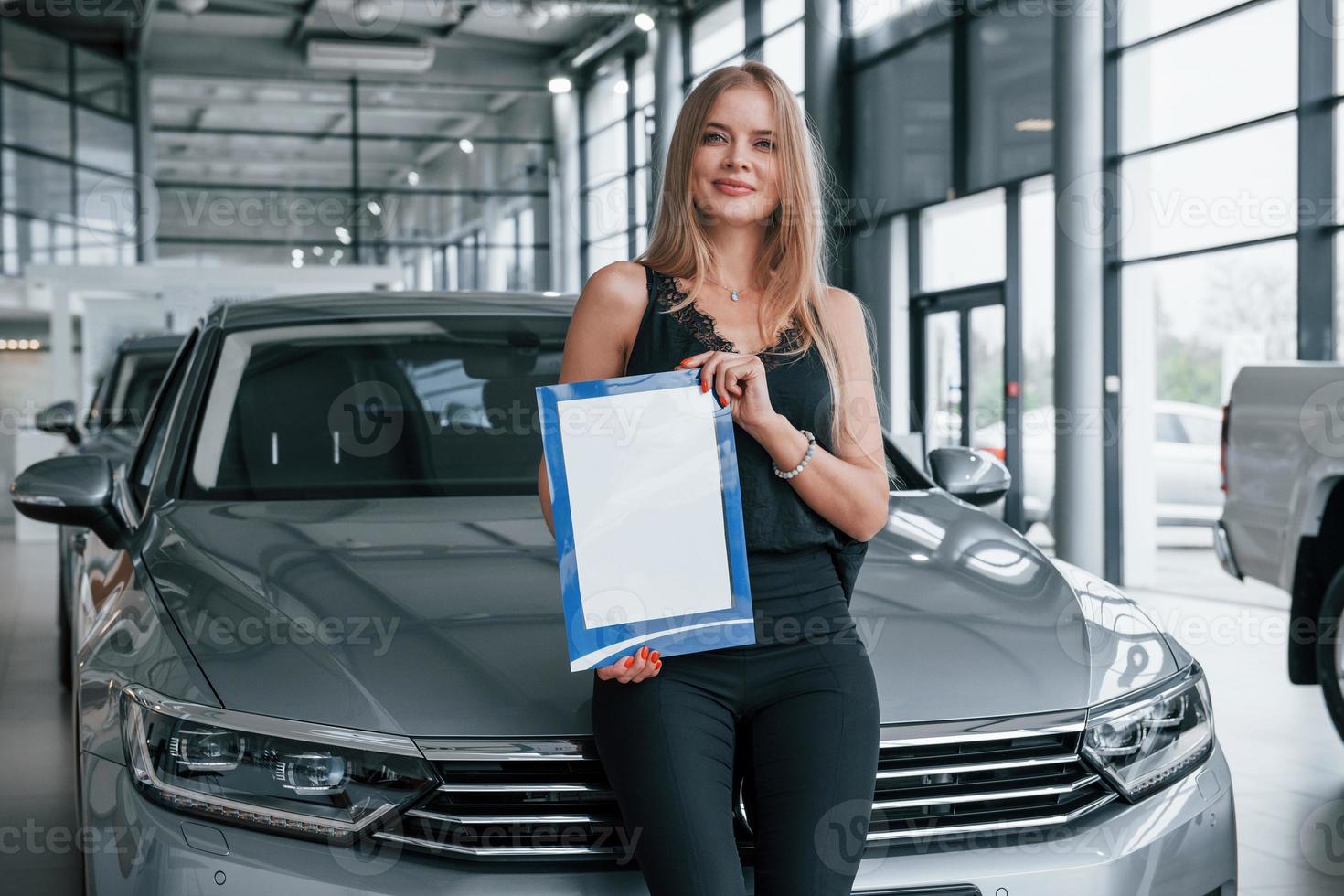 Successful woman. Girl and modern car in the salon. At daytime indoors. Buying new vehicle photo