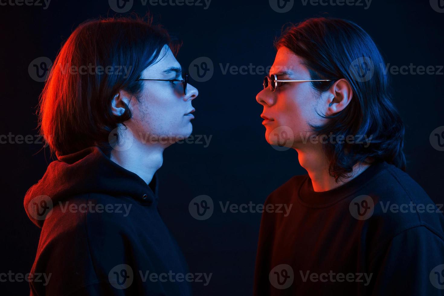 Looking at each other. Creative photo. Portrait of twin brothers. Studio shot in dark studio with neon light photo