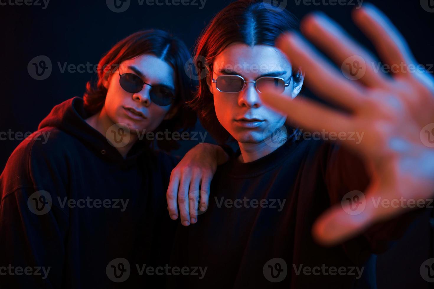 Showing the hand. Portrait of twin brothers. Studio shot in dark studio with neon light photo