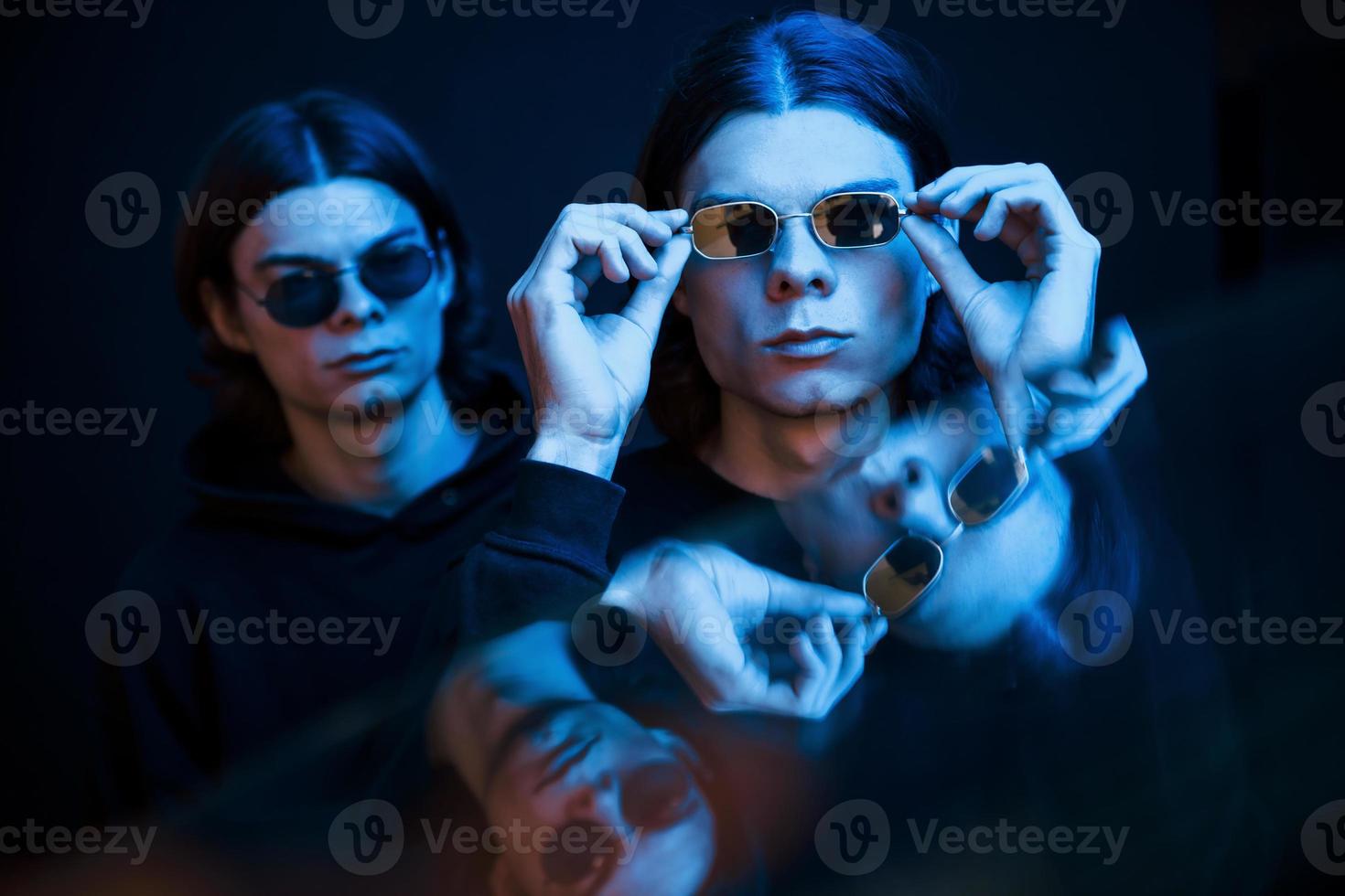 usando gafas de sol. retrato de hermanos gemelos. foto de estudio en estudio oscuro con luz de neón