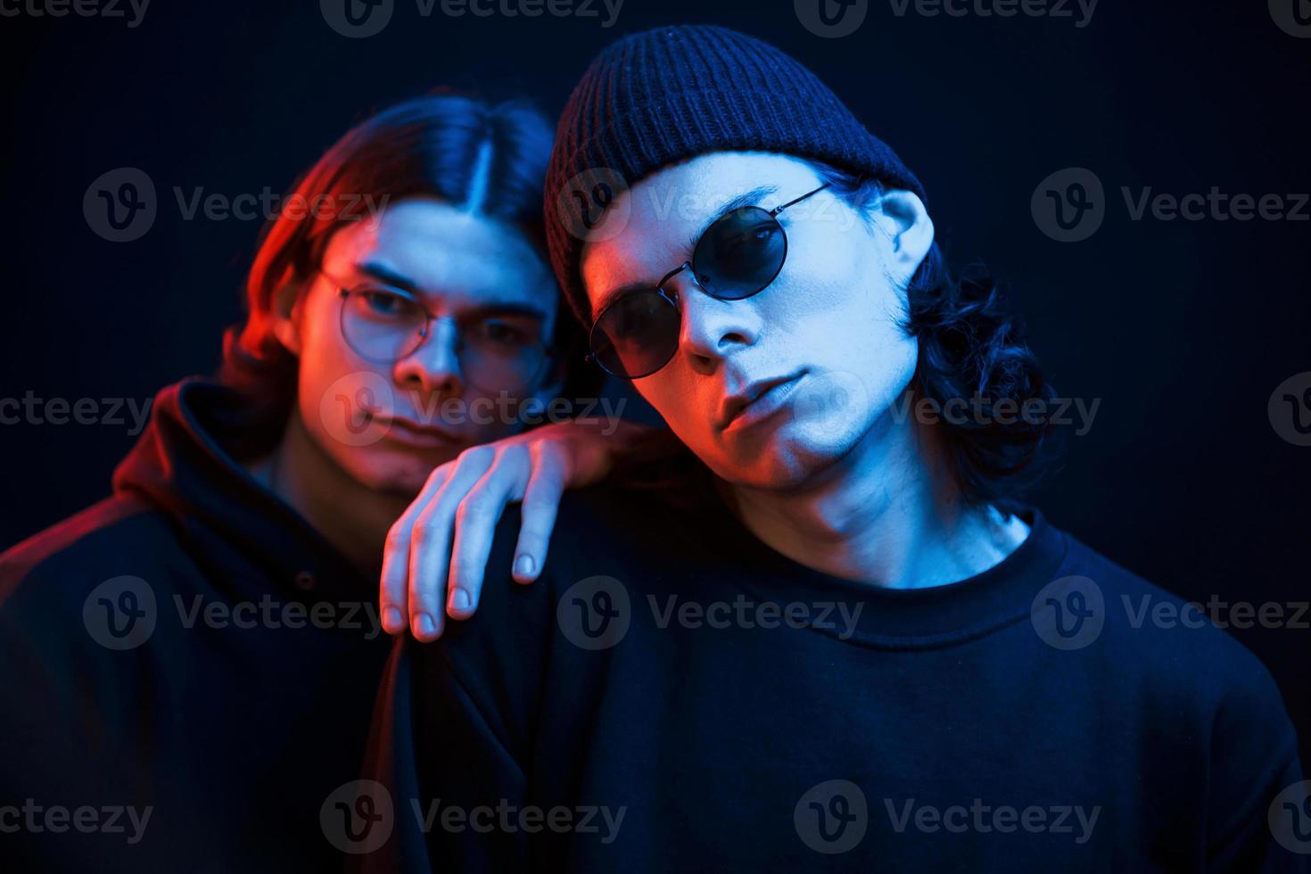 Leaning on the brother. Portrait of twins. Studio shot in dark studio with neon light photo