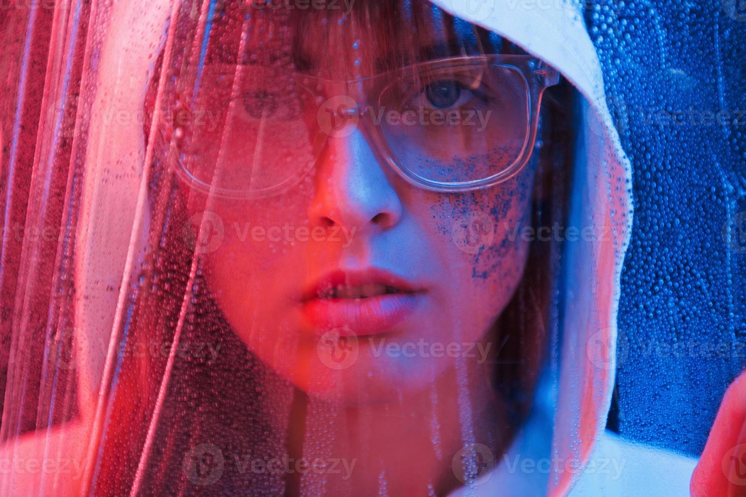 Looking through the wet material. Studio shot in dark studio with neon light. Portrait of young girl photo