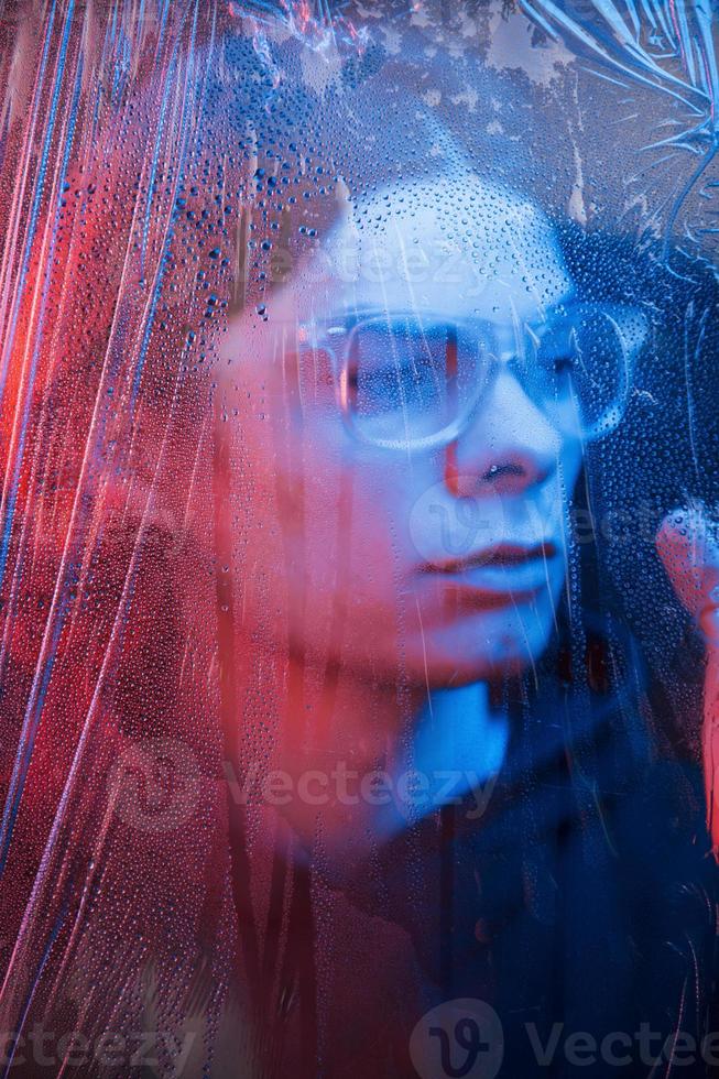 rostro humano borroso. foto de estudio en estudio oscuro con luz de neón. retrato de hombre serio detrás del vidrio mojado