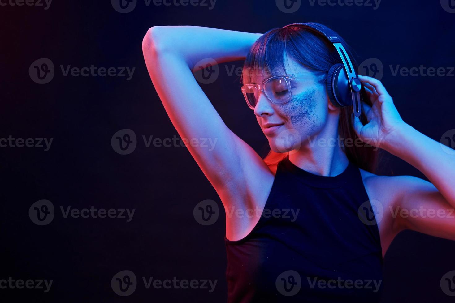 tocando los auriculares y escuchando la música. foto de estudio en estudio oscuro con luz de neón. retrato de niña