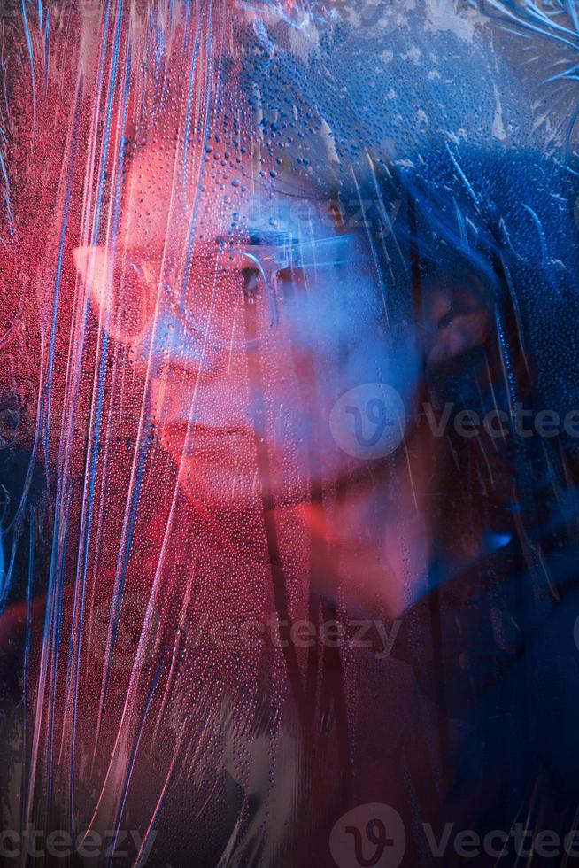 Side view. Studio shot in dark studio with neon light. Portrait of serious man behind the wet glass photo