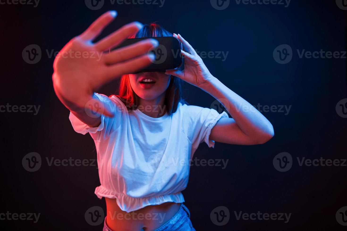 I wanna touch it. Young woman using virtual reality glasses in the dark room with neon lighting photo