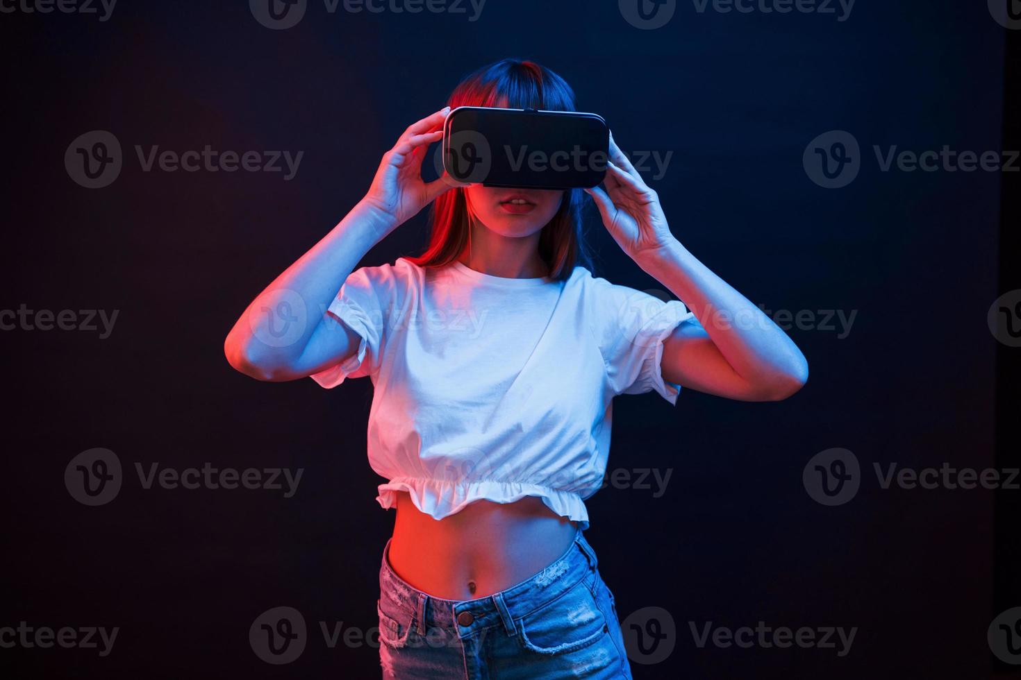 Impressed girl. Young woman using virtual reality glasses in the dark room with neon lighting photo