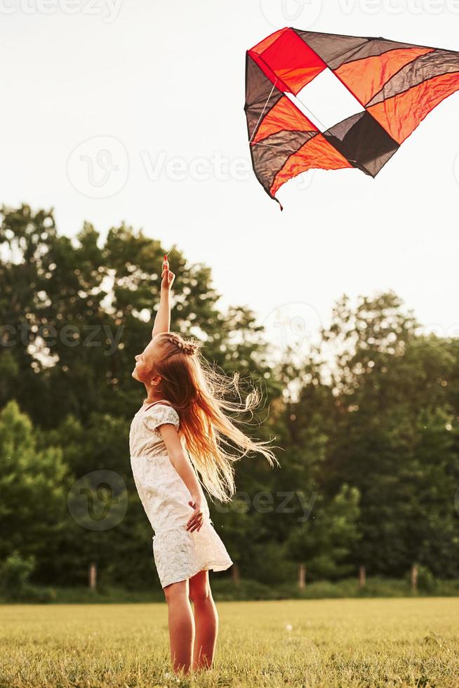 Feeling joy. Happy girl in white clothes have fun with kite in the field. Beautiful nature photo