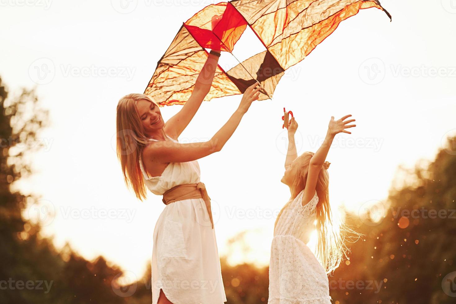 With hands up. Mother and daughter have fun with kite in the field. Beautiful nature photo