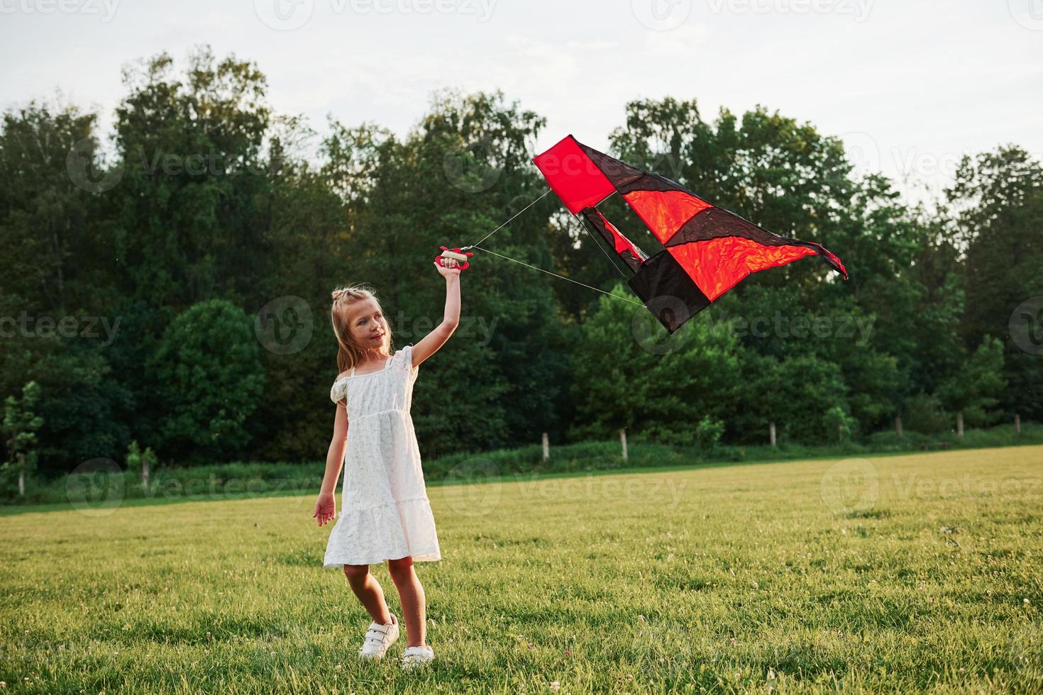 Red and black colored kite. Happy girl in white clothes have fun in the field. Beautiful nature photo