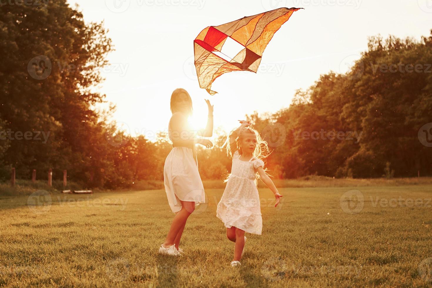 On short grass. Mother and daughter have fun with kite in the field. Beautiful nature photo