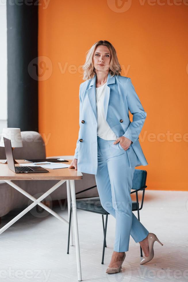 Female general manager. Businesswoman with curly blonde hair indoors in room with orange colored wall and wooden table photo