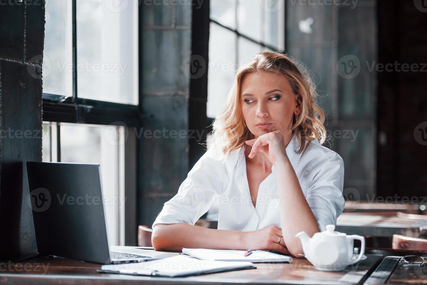 Waits when file will open. Businesswoman with curly blonde hair indoors in cafe at daytime photo