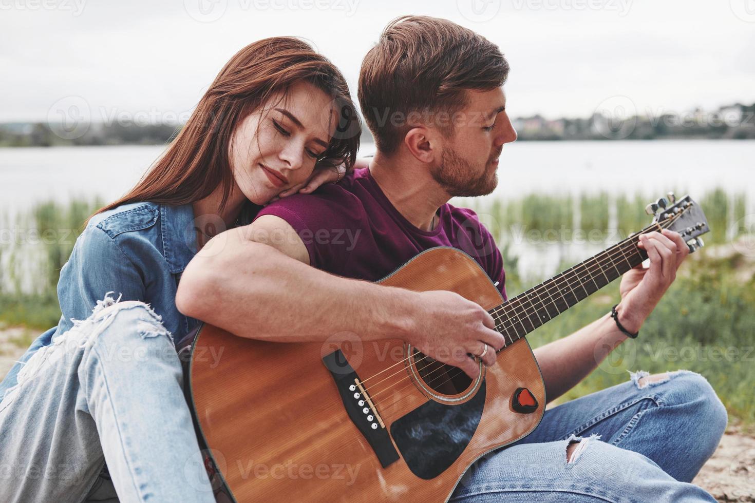 Feeling good. Man plays guitar for his girlfriend at beach on their picnic at daytime photo